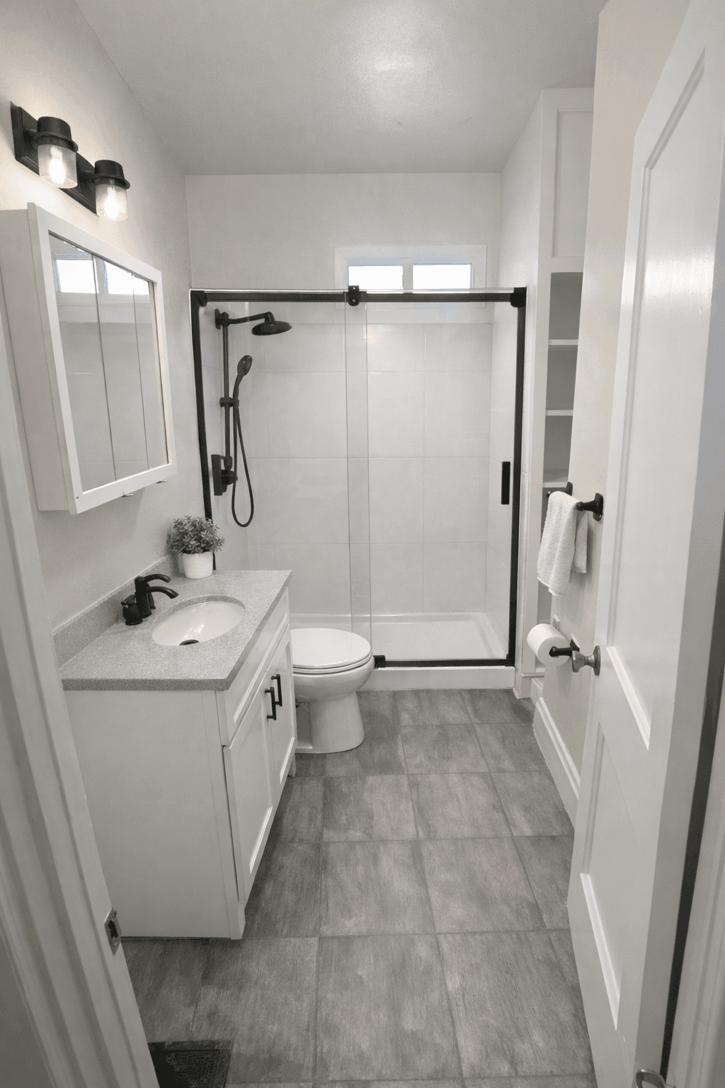 Modern bathroom with white vanity, grey tile floor, and a black-framed glass shower.