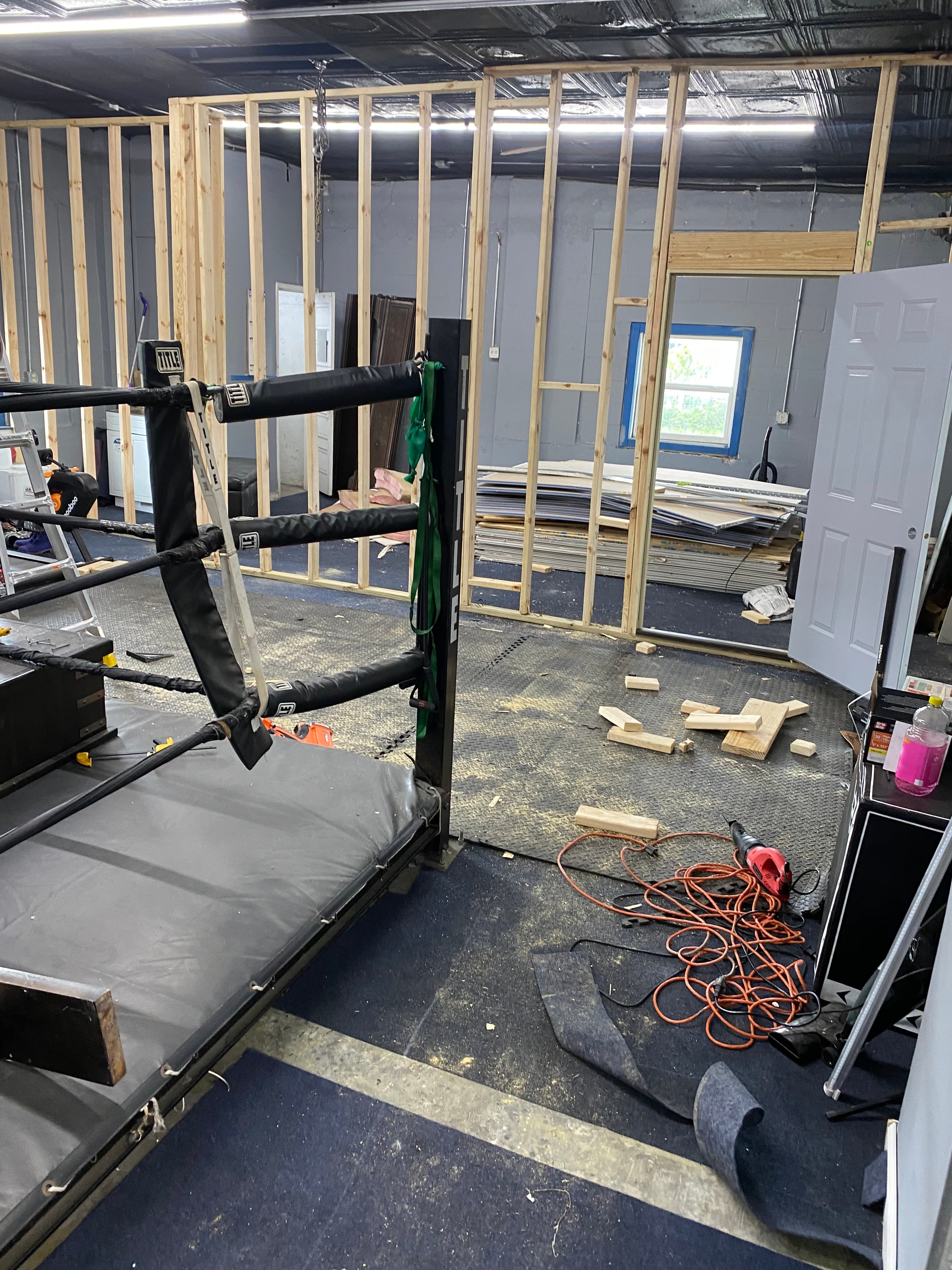Boxing ring corner in a room with wooden wall framing, tools, and construction debris.