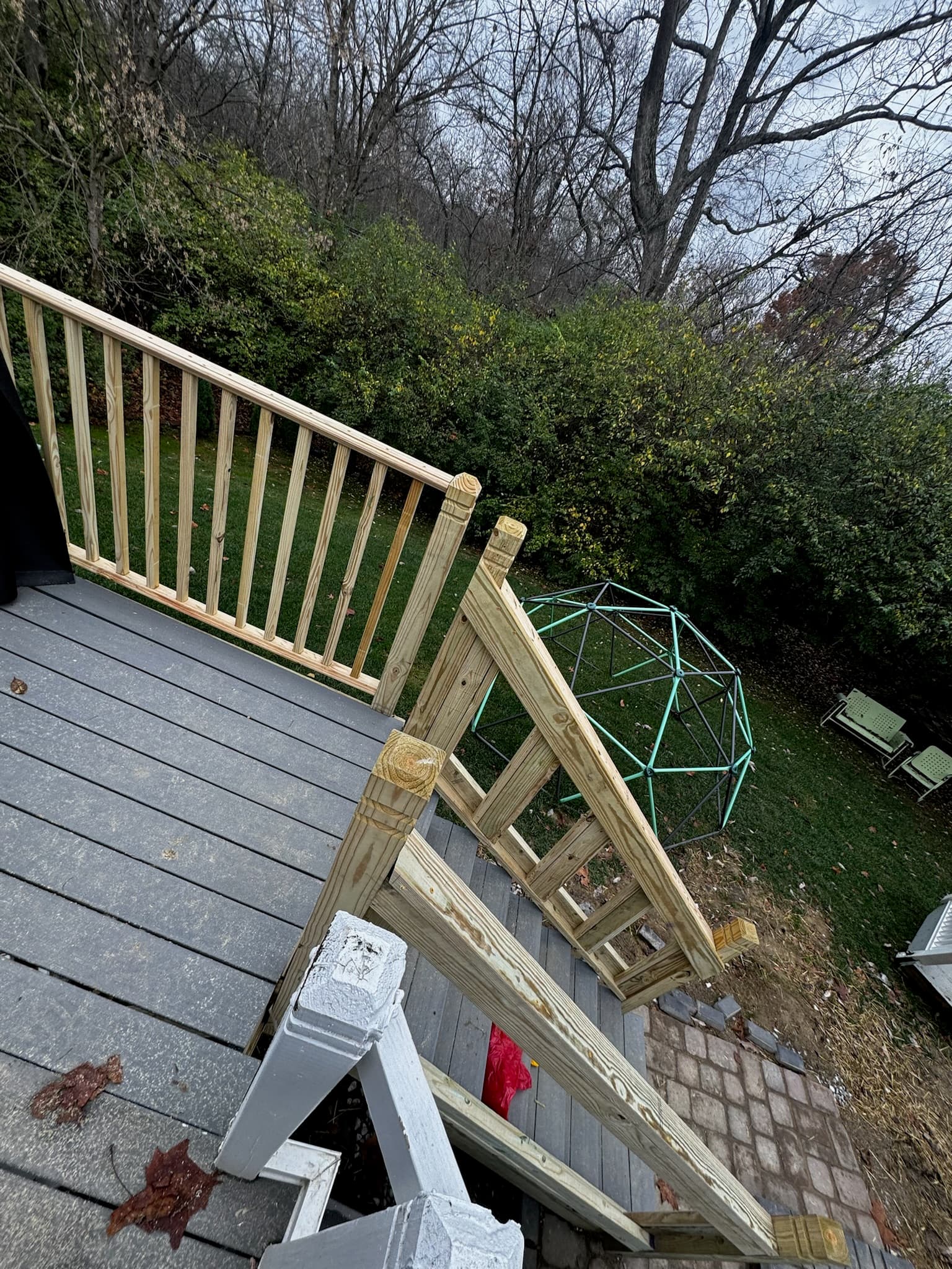 Grey deck with wooden railings overlooking a backyard with a green geodesic climbing dome.