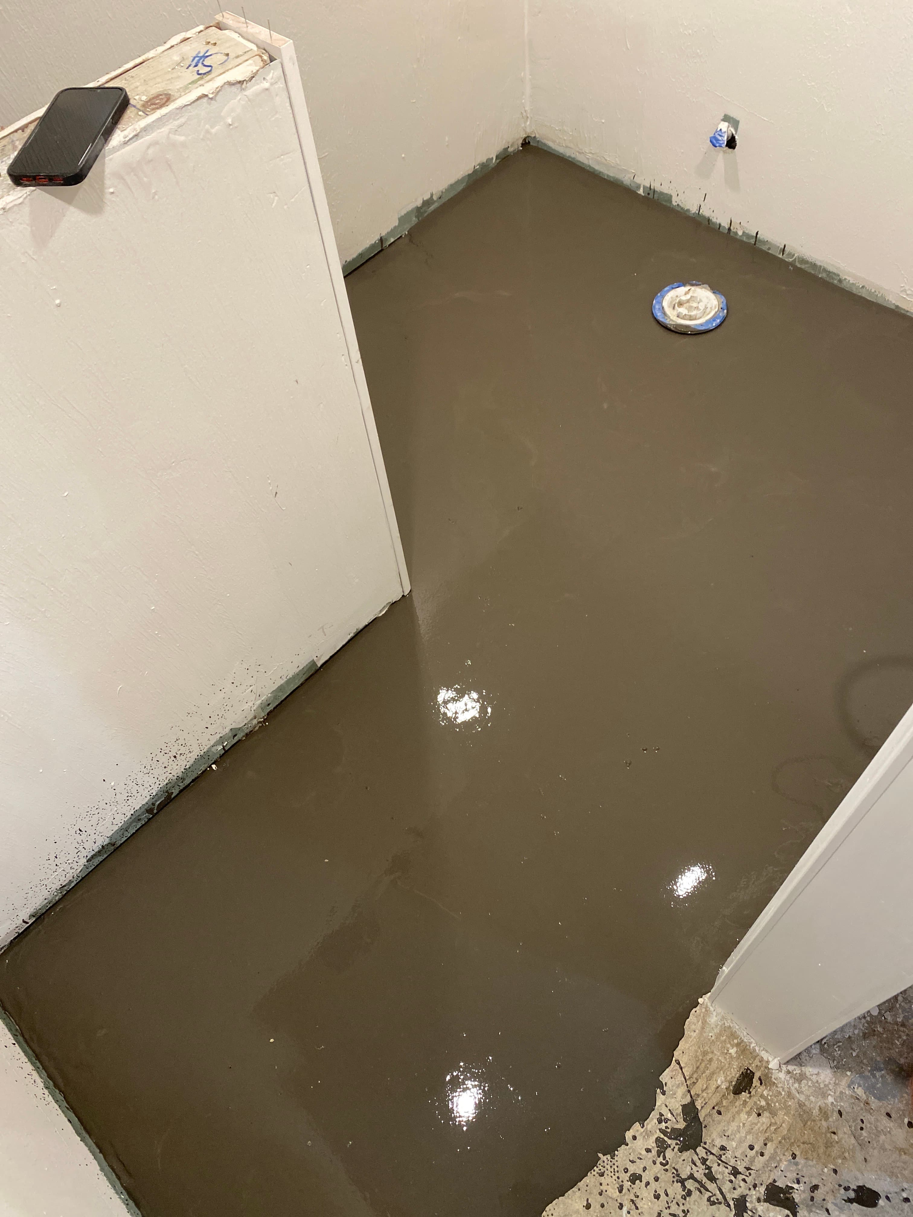 Wet, glossy dark gray floor leveling compound in a room with white walls during renovation.